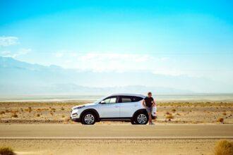 man standing beside white SUV near concrete road under blue sky at daytime