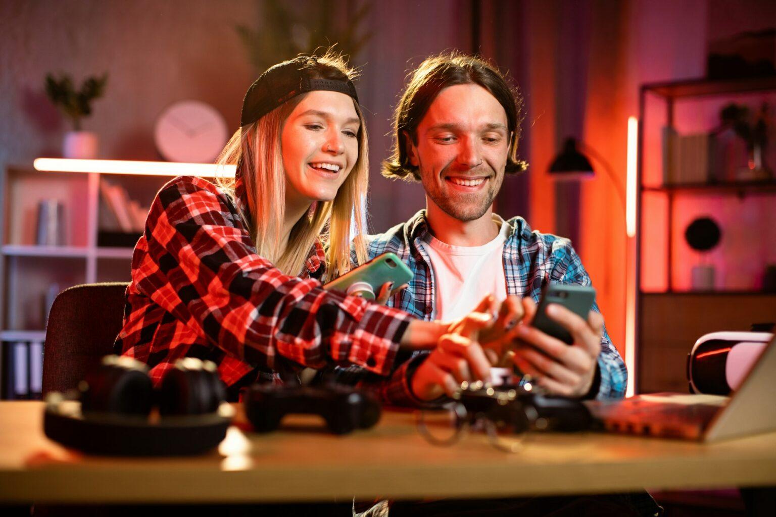 Young happy couple sit in kitchen at table looking at smartphone screen