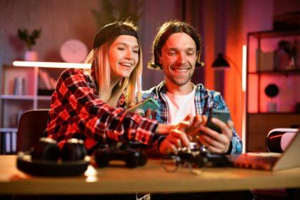 Young happy couple sit in kitchen at table looking at smartphone screen