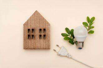 Wooden house with LED light bulb, electric plug and green leaves, electricity prices and energy