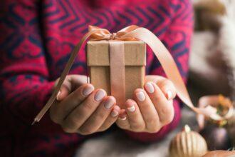 A woman holding a Christmas gift with a ribbon on a wooden table. Christmas presents and New Year