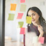 Business female employee with many conflicting priorities arranging sticky notes commenting and