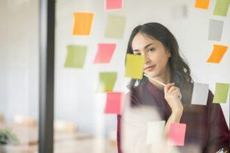 Business female employee with many conflicting priorities arranging sticky notes commenting and