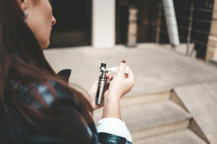 Woman refills liquid in e-cigarette closeup. Girl refills liquid in vape. Electronic cigarette