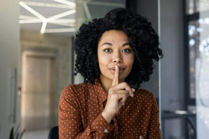 Young woman gestures for silence in a modern office setting