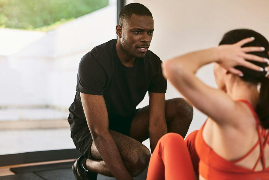 Black trainer helping woman doing crunches in gym