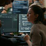 Junior programer sitting down on desk showing laptop with source code to senior dev