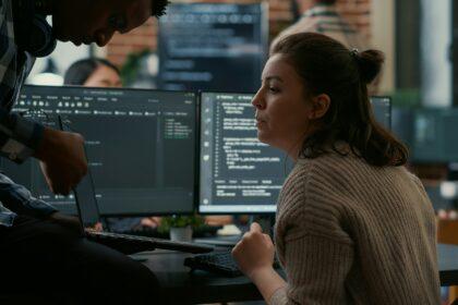 Junior programer sitting down on desk showing laptop with source code to senior dev