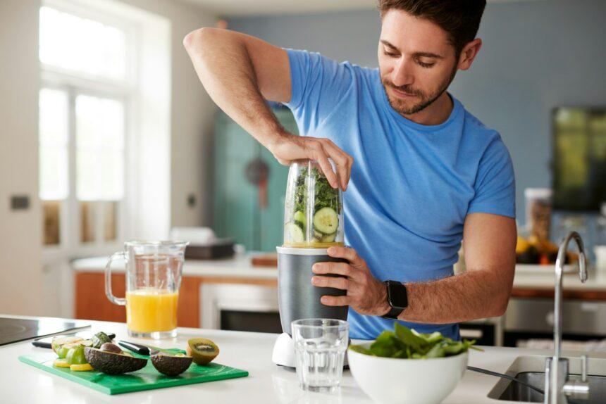 Man Making Healthy Juice Drink With Fresh Ingredients In Electric Juicer After Exercise