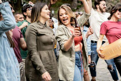 Two curvy girls are having a blast dancing and drinking beer at a pool party.