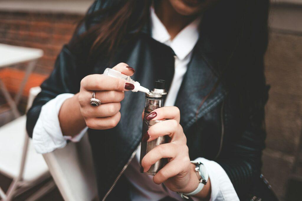 Woman refills liquid in e-cigarette closeup. Girl refills liquid in vape. Electronic cigarette