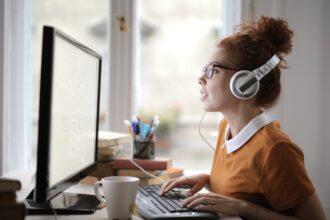 Young woman with headphones and glasses working on the computer under the lights in a house