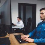 Side view, two programmers working in the office coding on desk top computers