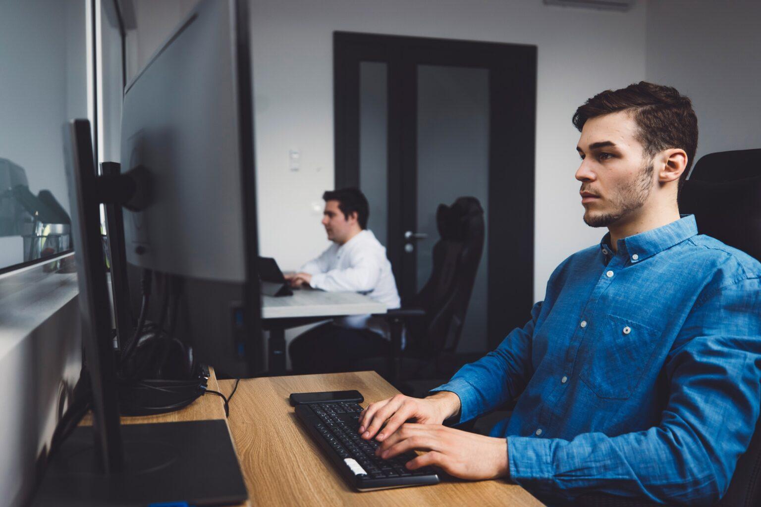 Side view, two programmers working in the office coding on desk top computers