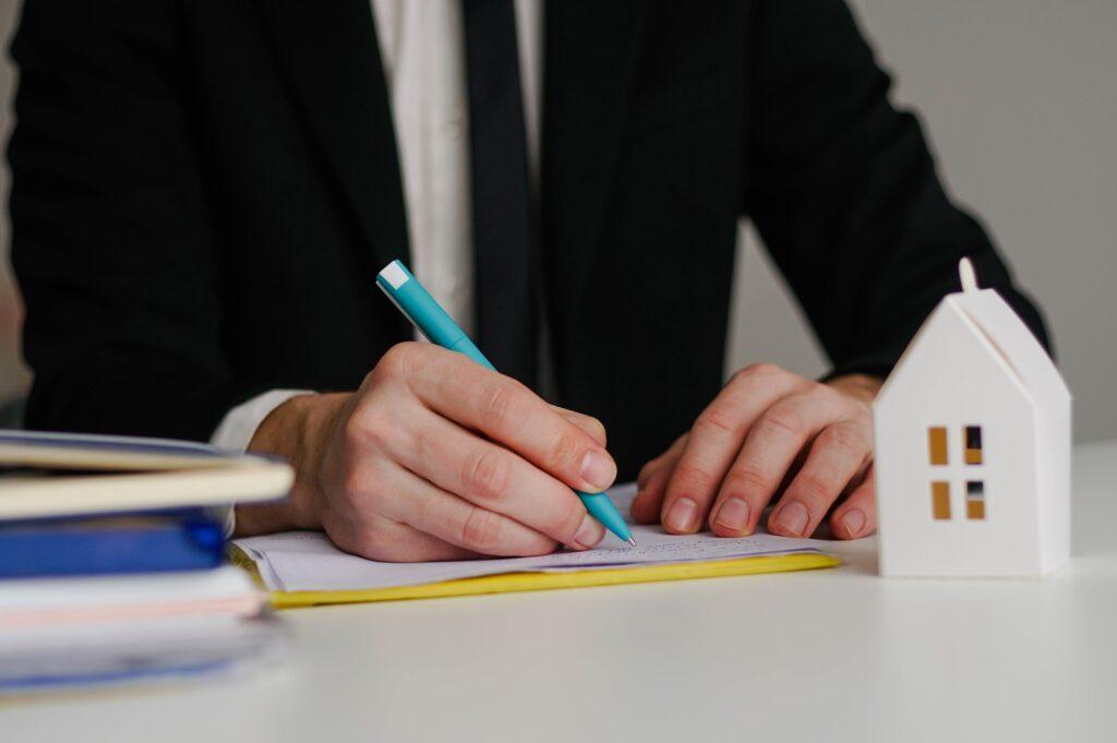 Close up of real estate agent sign contract for home loan insurance with paper house model.