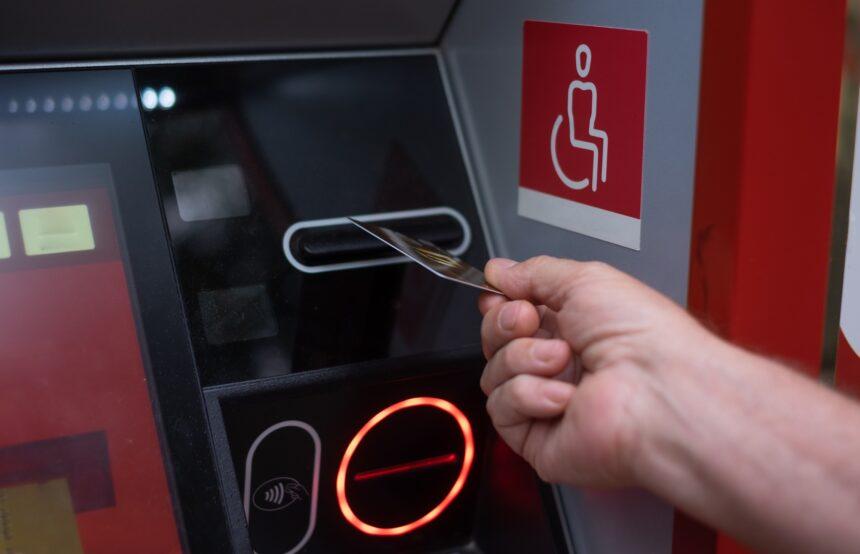 Woman hand inserting ATM credit card into bank machine to transfer money or withdraw