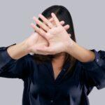 Woman in black suit showing her denial with no on her hand against gray background