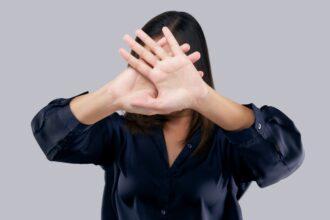 Woman in black suit showing her denial with no on her hand against gray background