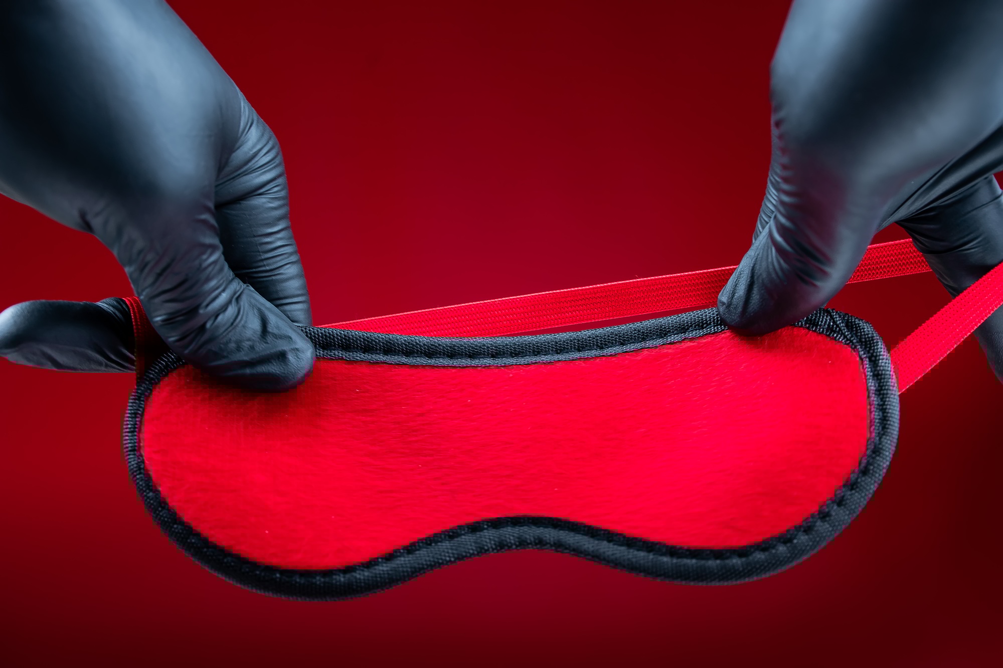 hands in black gloves holding a red erotic bandage for bdsm games