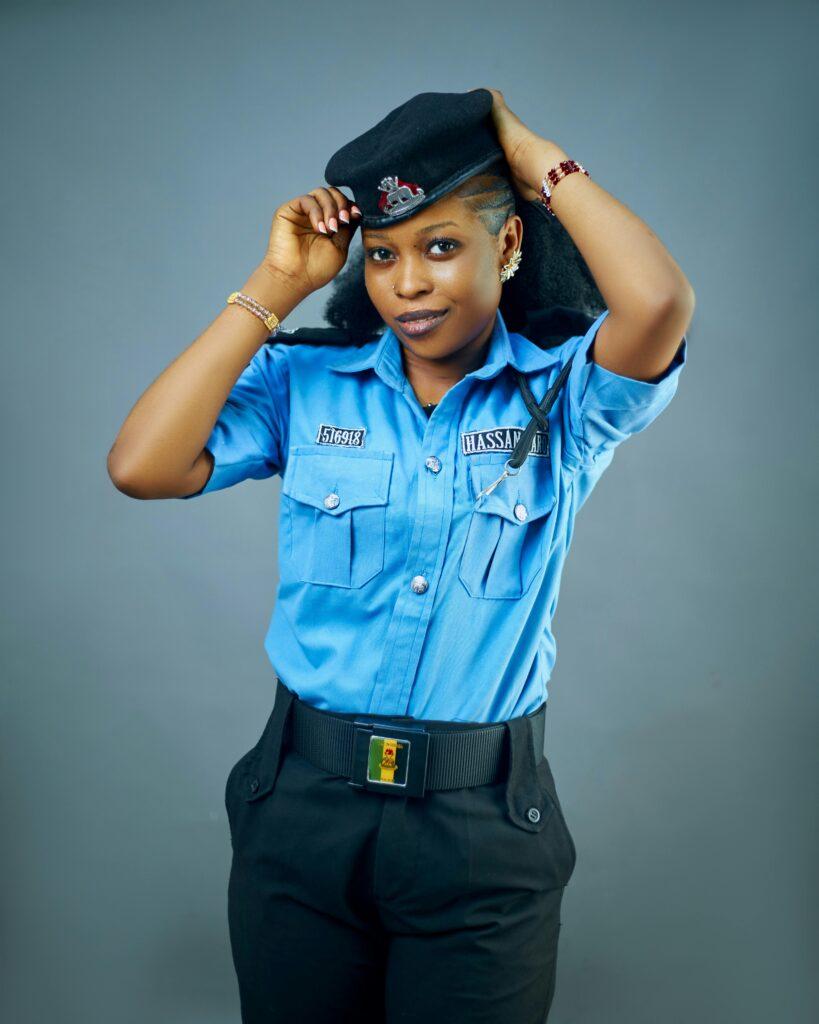 Portrait of a female police officer adjusting her cap, wearing a blue uniform against a neutral background.