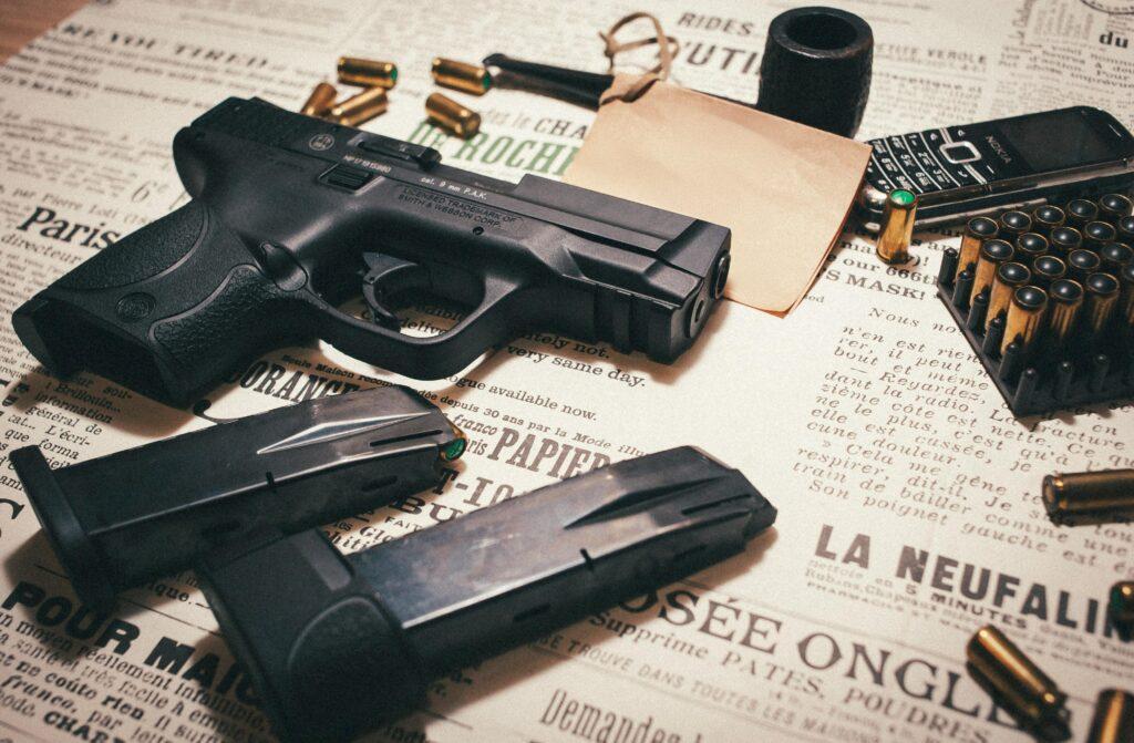 Shein échappe à la suspension mais demeure étroitement surveillé A black handgun with ammunition and phone on a newspaper-themed surface.