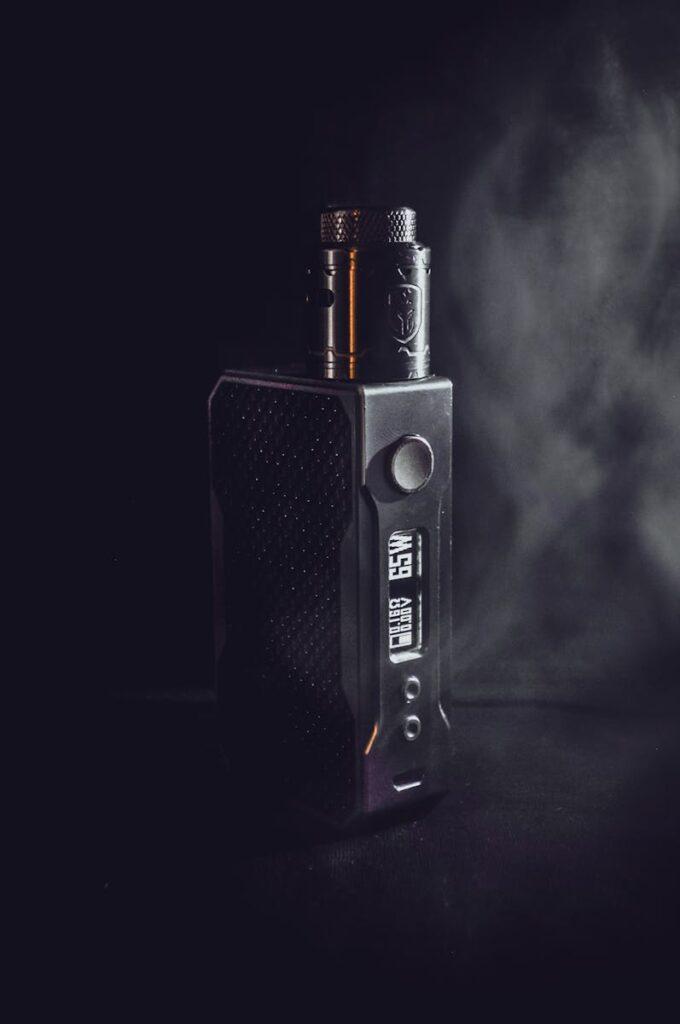 Votre premier e-liquide : pourquoi tant de vapoteurs débutants se trompent Dark and atmospheric close-up of a vape mod with subtle smoke in the background.