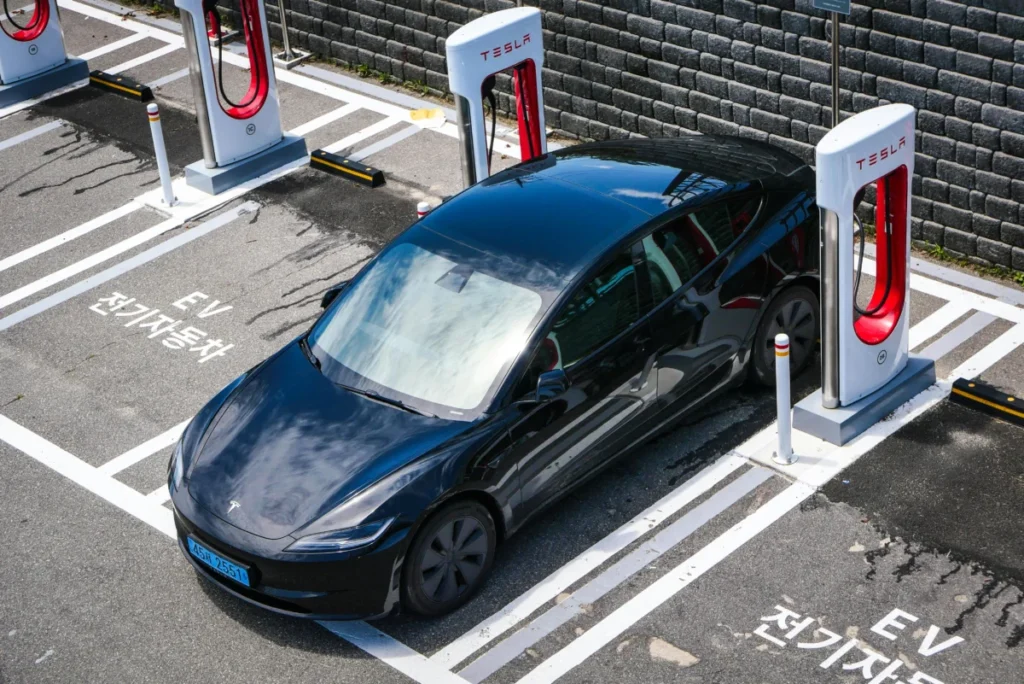 A black Tesla parked at a charging station in an urban setting.