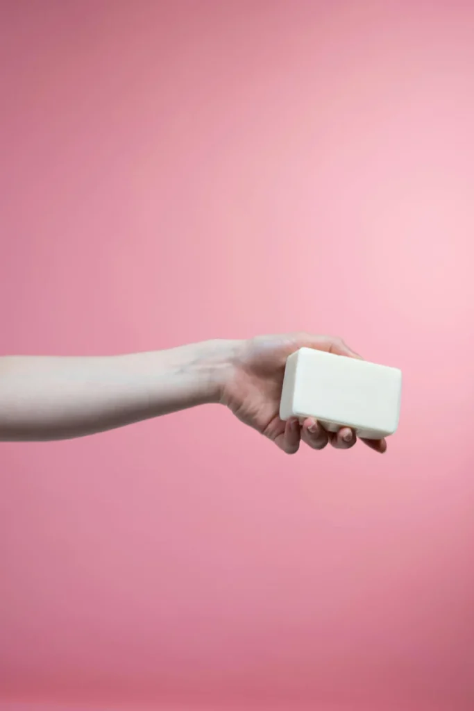 A hand holding a bar of soap with a pink background, symbolizing hygiene and cleanliness.