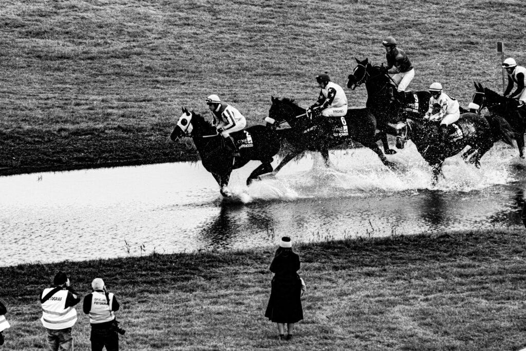 Black and white capture of a thrilling horse race water jump in Wrocław, Poland.