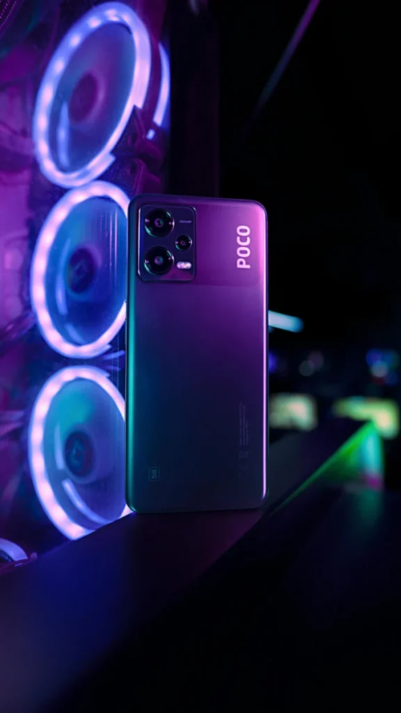Poco smartphone displayed vertically with a neon lit gaming setup in the background.