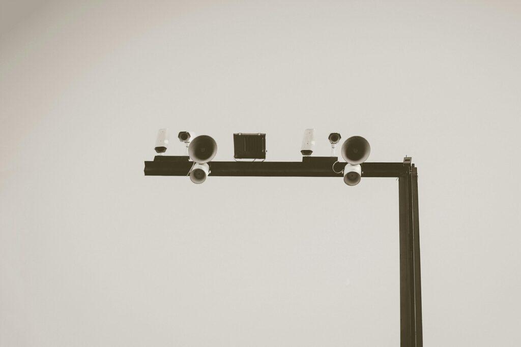 Monochrome image of CCTV cameras and speakers on an outdoor metal frame in Barcelona.