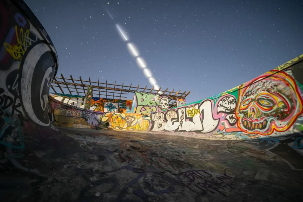 Dynamic view of a graffiti-covered skate park under a starry night sky with light trails.