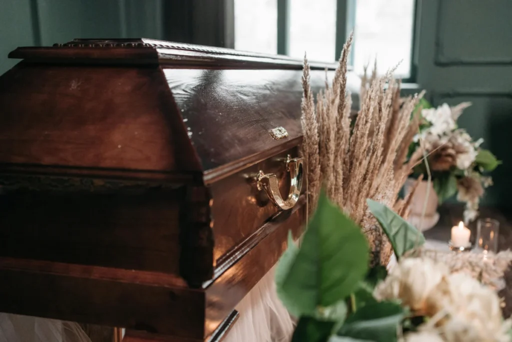 A beautiful funeral display featuring a wooden coffin with flowers and candles indoors.